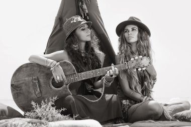İki güzel boho kız yastık çadır, oturup gitar ile