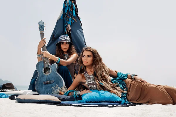 สาวยิปซีสวยสองคนพร้อมกีตาร์นั่งบนหมอนที่เทป รูปภาพสต็อกที่ปลอดค่าลิขสิทธิ์