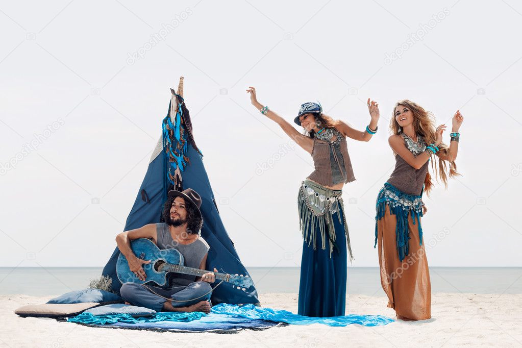 Attractive boho man playing guitar and two girls dancing outdoor