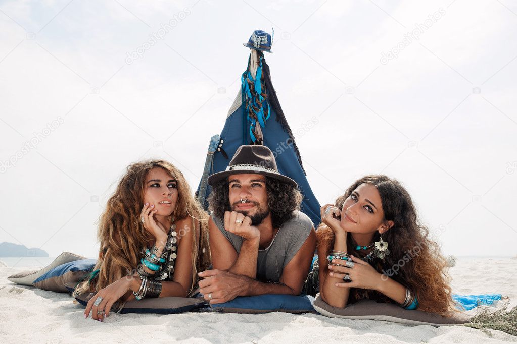 Attractive boho man and women sitting on pillows at tepee on bea