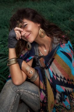 Yeşil alanında oturup panço giyen güzel boho kadın