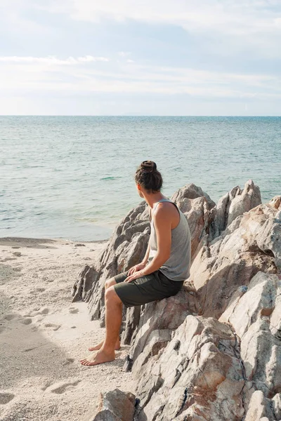 Jonge man zittend op het strand en kijk op de horizon lijn — Stockfoto