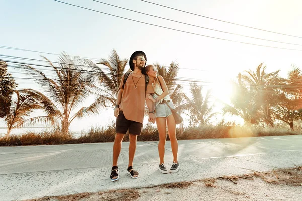 Feliz pareja alegre caminando por la carretera en la isla tropical al atardecer —  Fotos de Stock