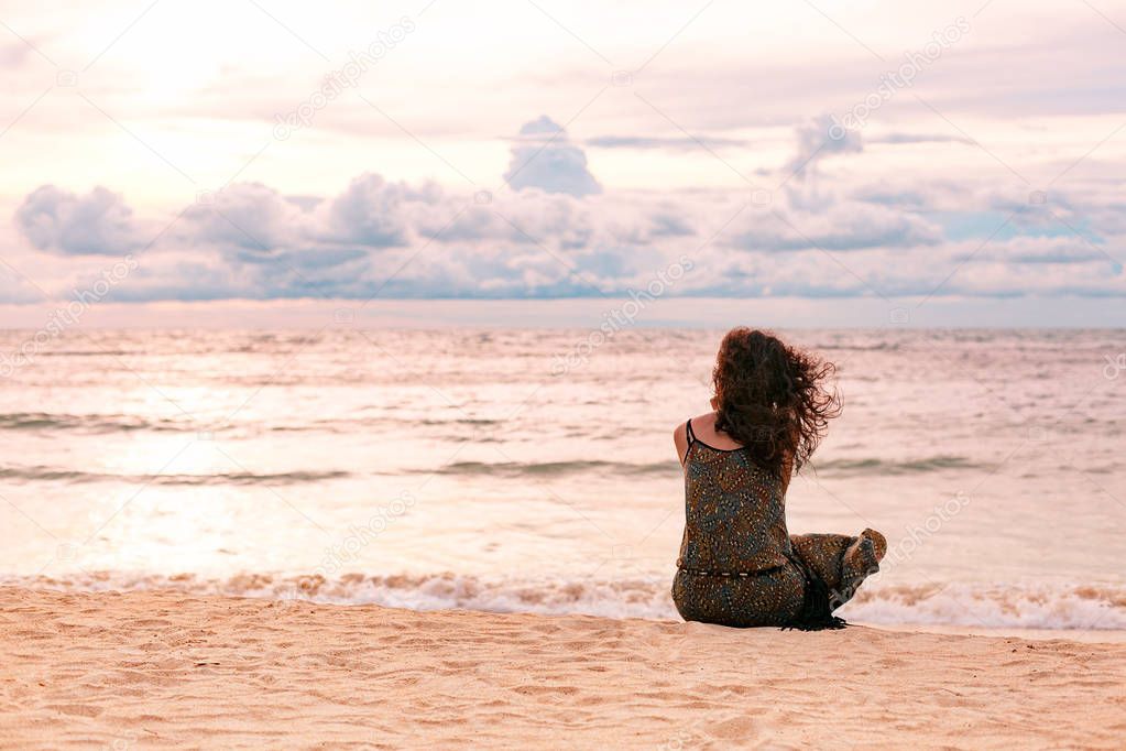beautiful young woman sitting on the beach at sunset time