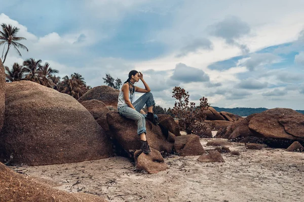 Modelo joven estilo boho sentado en una piedra en la playa — Foto de Stock