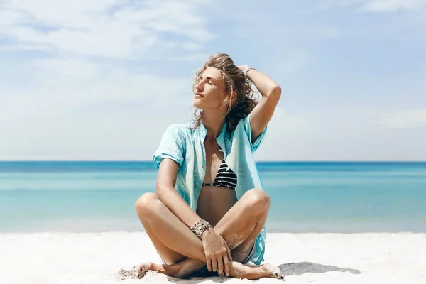 Bela jovem mulher alegre em biquíni sentado na praia — Fotografia de Stock