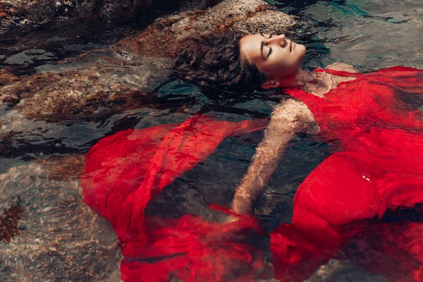 Bela jovem mulher em vestido vermelho que coloca dowm na água — Fotografia de Stock