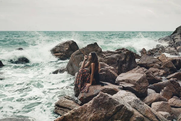 Bela jovem boho estilo mulher sentada em uma praia de pedra — Fotografia de Stock