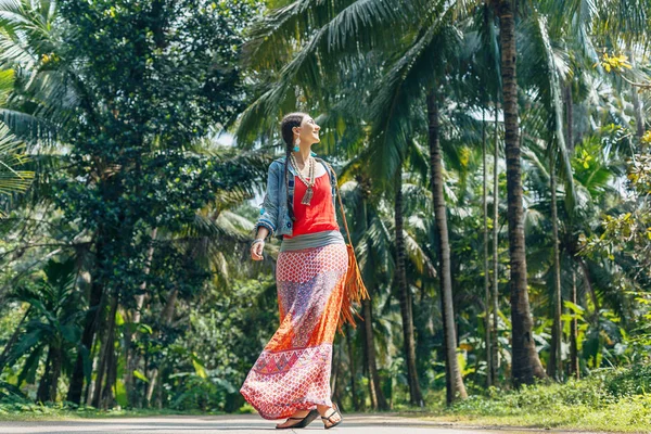 Allegro giovane donna in stile boho che cammina lungo la strada con tropica — Foto Stock