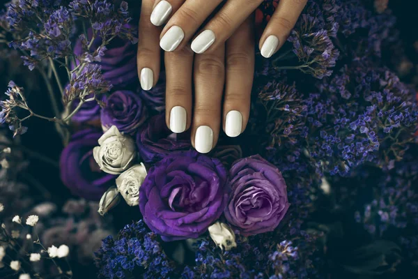 Vrouw handen met manicure op rozen op achtergrond — Stockfoto