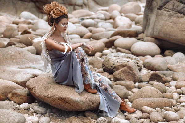 Young fashionable woman sitting on the stone beach — Stock Photo, Image