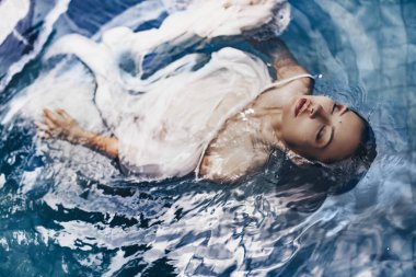 Kumaş giymiş, suda poz veren güzel bir kadının moda çekimi.