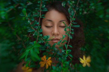 Yeşil yapraklarla poz veren çekici genç kadın.