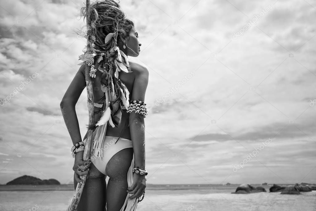 Attractive wild boho woman in native american style and white clothes posing at beach