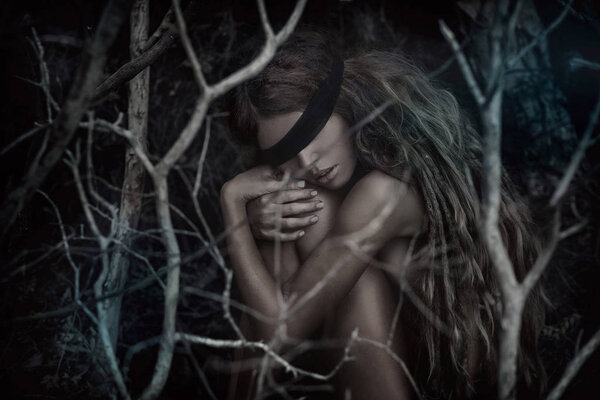 Young beautiful blindfolded woman in dark spooky forest