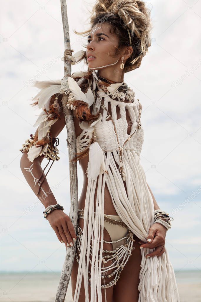 Attractive wild boho woman in native american style and white clothes posing at beach