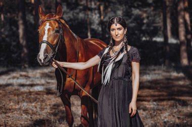 Bohem kadın ormanda atlarla birlikte poz veriyor.