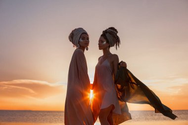 two young beautiful girls in turban on the beach at sunset  clipart