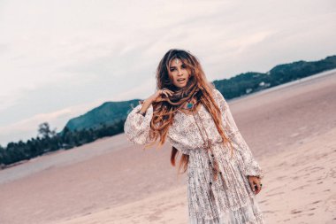 Gün batımında sahilde poz veren neşeli boho kadın.