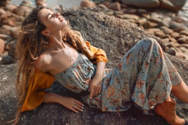 Güzel taş sahilde poz veren çekici boho kızı.
