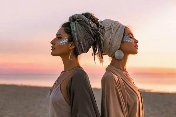 Dwie młode piękne dziewczyny w Turban na plaży o zachodzie słońca — Zdjęcie stockowe