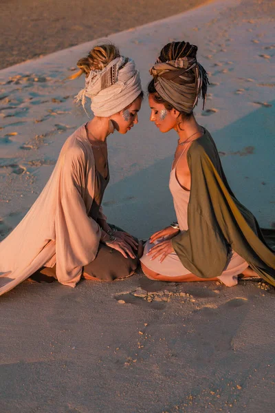 Dos chicas hermosas jóvenes en turbante en la playa al atardecer — Foto de Stock