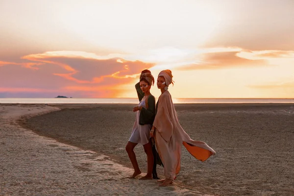 Duas meninas bonitas jovens em turbante na praia ao pôr do sol — Fotografia de Stock