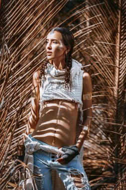 Kuru palmiye yapraklarının arkasında poz veren genç ve güzel bir kadın.
