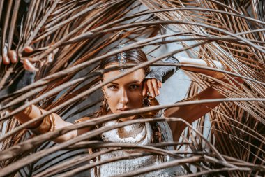 Kuru palmiye yapraklarının arkasında poz veren genç ve güzel bir kadın.