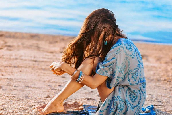 美丽的年轻时髦女人坐在海滩上 日落时用她的头发玩耍 — 图库照片