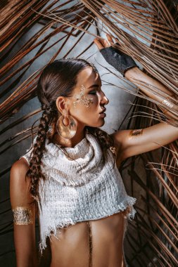 Kuru palmiye yapraklarının arkasında poz veren genç ve güzel bir kadın.