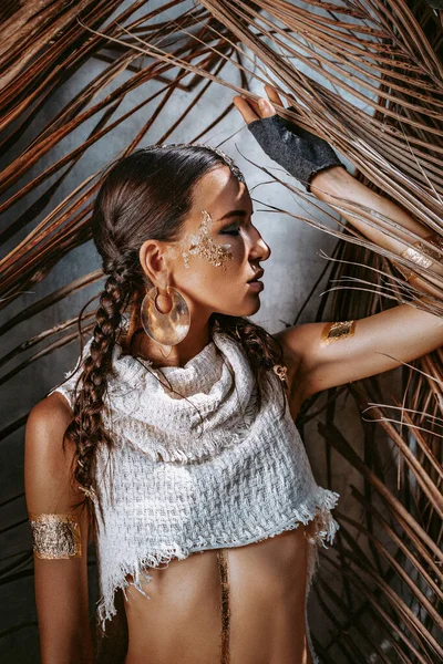 Kuru palmiye yapraklarının arkasında poz veren genç ve güzel bir kadın.