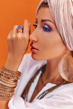 Turuncu arka planda boho aksesuarları olan güzel, genç ve şık bir kadın.