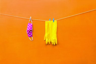 Yüz maskesi ve sarı eldivenler turuncu arka plandaki mandallara asılı ve kuru.