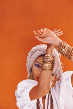 Turuncu arka planda boho aksesuarları olan güzel, genç ve şık bir kadın.