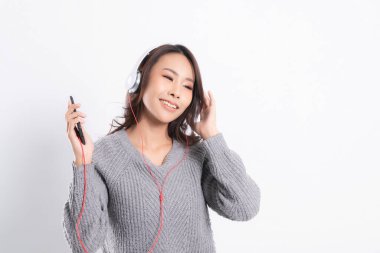 Gri kazak giyen genç güzel bir kadın yalan söylüyor ve beyaz arka planda izole edilmiş beyaz kulaklıklar takarak müzik dinliyor. Rahatlatıcı ve mutlu.