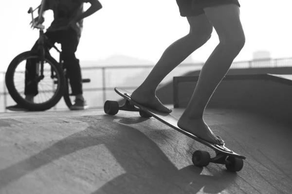 Barefoot boy going down skate ramp while another with a BMX in t — Stock Photo, Image