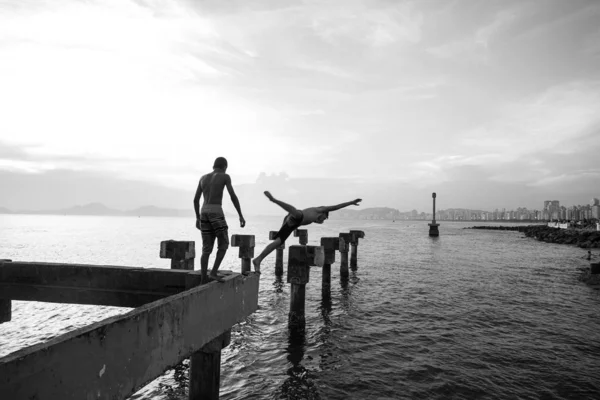 Dois meninos carentes jogando salto no mar de um velho cais destroye — Fotografia de Stock