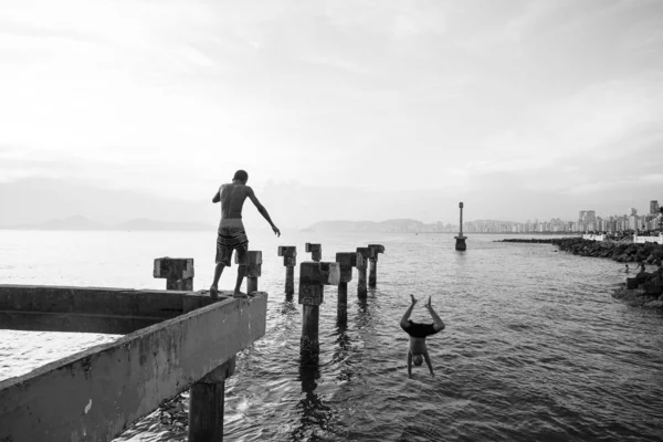 Dois meninos carentes jogando salto no mar de um velho cais destroye — Fotografia de Stock