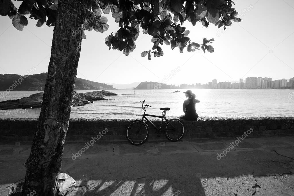 Cyclist, wearing safety mask, seated enjoying the sunset in Sao Vicente during the coronavirus quarantine (COVID-19).