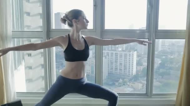 Молодая женщина практикует йогу дома с городским пейзажем — стоковое видео