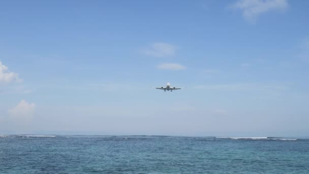 Avião pousando na ilha Aeroporto de Bali sob o mar azul com ondas no horizonte — Vídeo de Stock