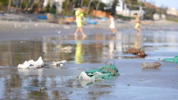Tiro estático de jugar a los niños en desenfoque en la playa contaminada por la basura, basura — Vídeos de Stock