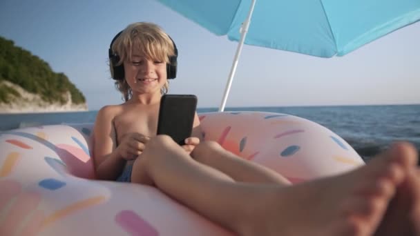 Cute child listening music on smart phone and singing on beach — Stock Video