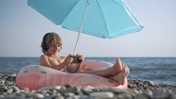 Мила дитина слухає музику на смартфоні на пляжі — стокове відео