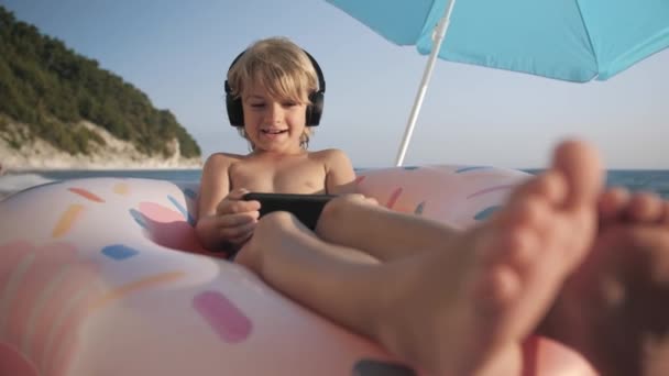 Lindo niño chats de vídeo en el teléfono inteligente en la playa — Vídeo de stock