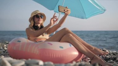 Güzel kız sahilde akıllı telefonuyla selfie çekiyor.