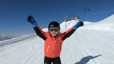 Smiling child skiing and waving hand on snow mountain
