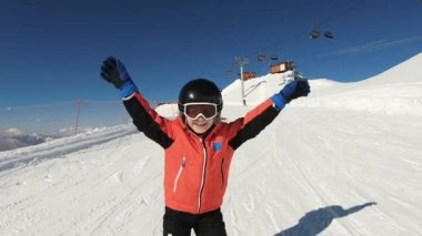 Smiling child skiing and waving hand on snow mountain