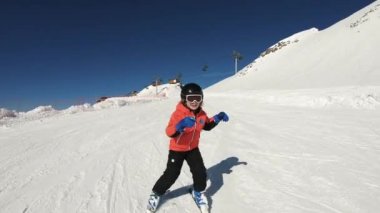 Smiling child skiing and waving hand on snow mountain